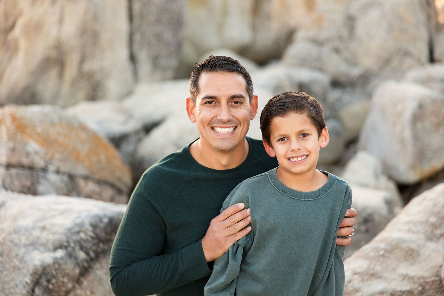 Portrait of parent and child in matching green sweaters smiling against rocky background.