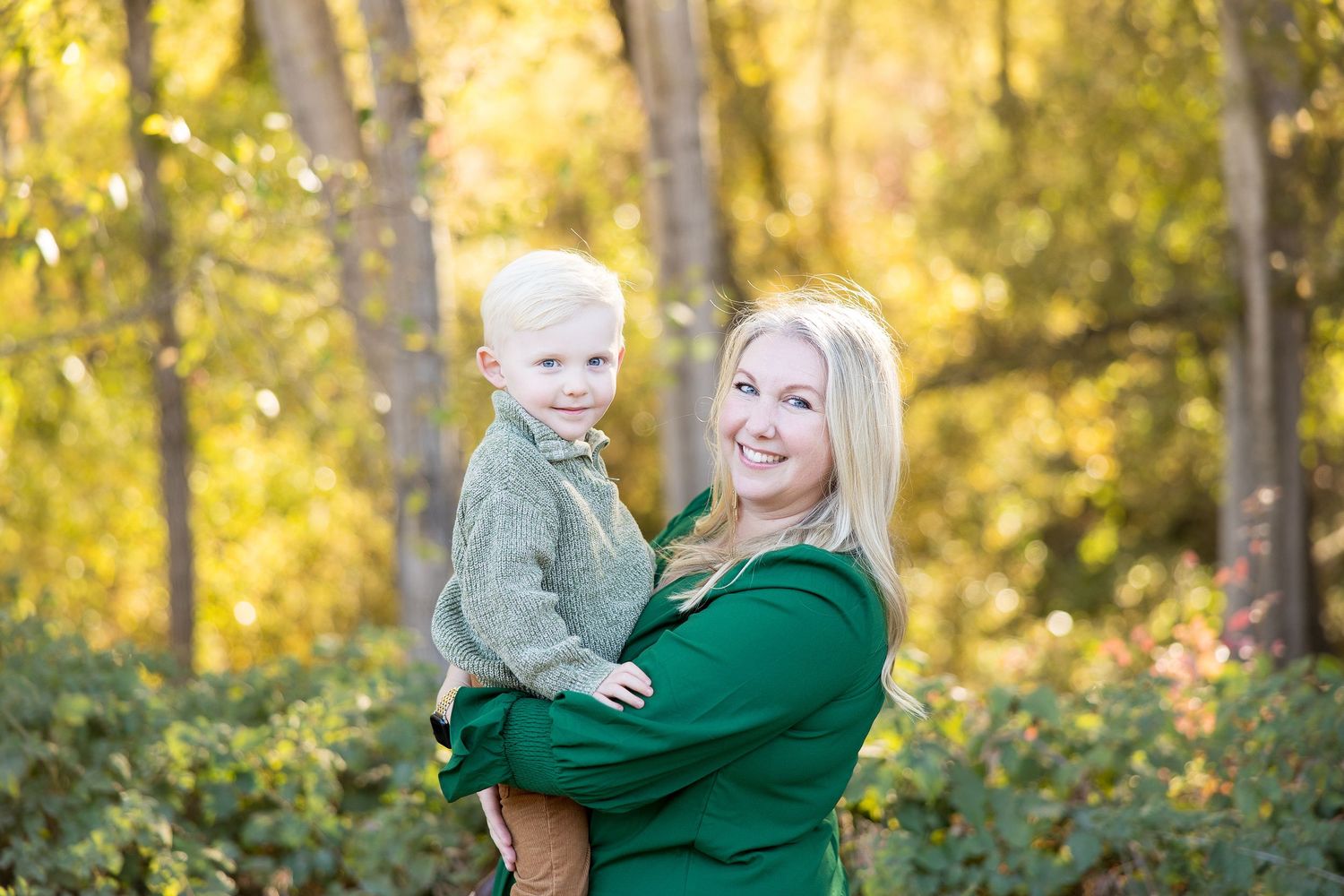 Beautiful autumn family photoshoot with coordinated green and brown outfits in a wooded setting.