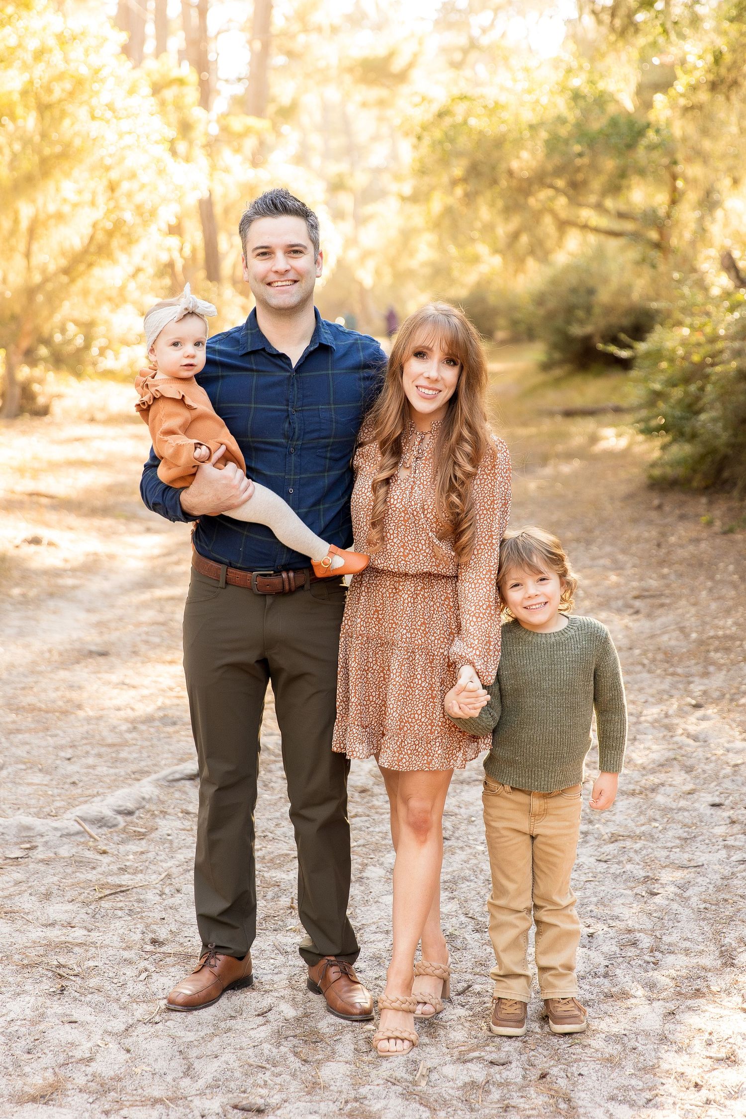 Family portrait in autumn setting with warm golden lighting and casual attire.