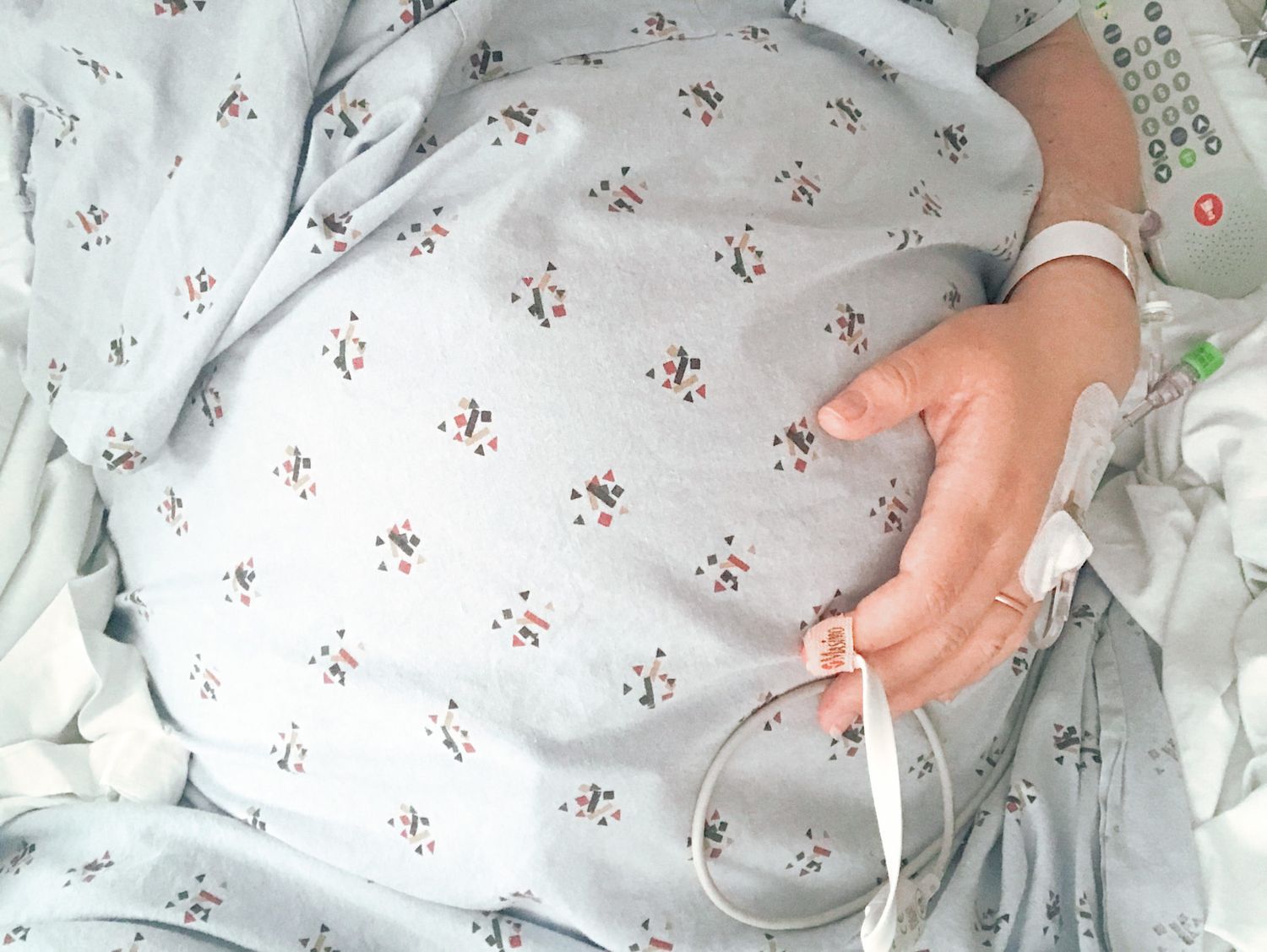 A baby wearing a white floral print sleeper reaches out with tiny hands against a matching patterned background.