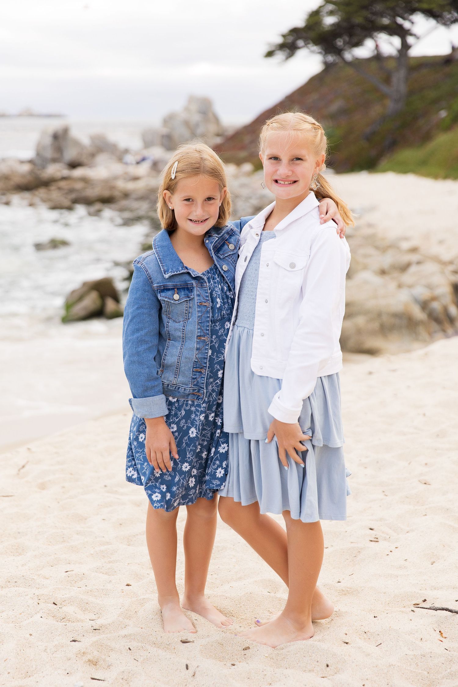 Two children in blue and white outfits play barefoot on a sandy beach.