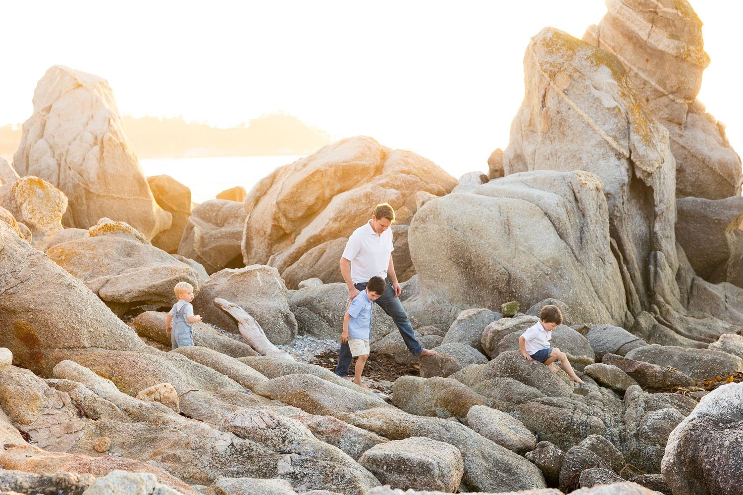 People explore large rocky formations on a beach during sunset.