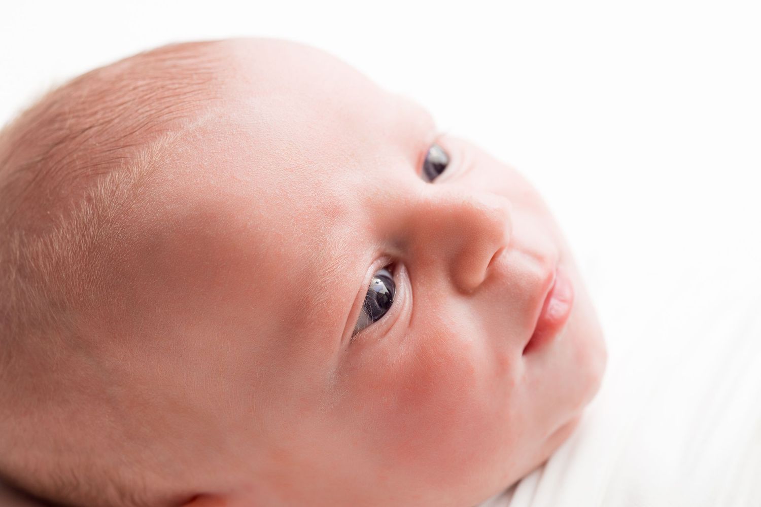 A newborn baby's face is shown in close-up profile view against a white background.