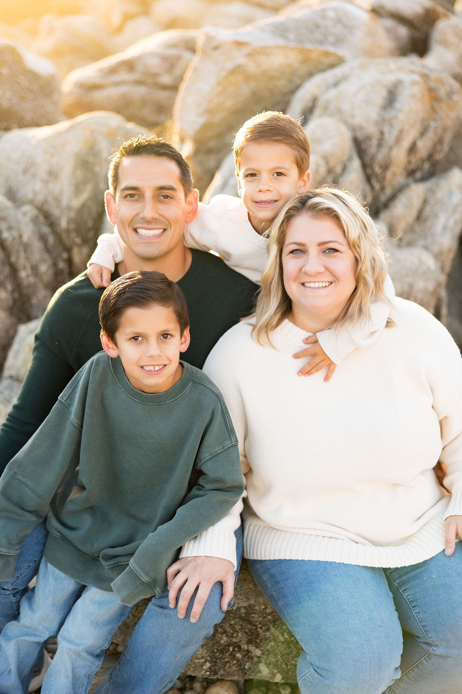 Family of four in coordinating sweaters posing together on coastal rocks.