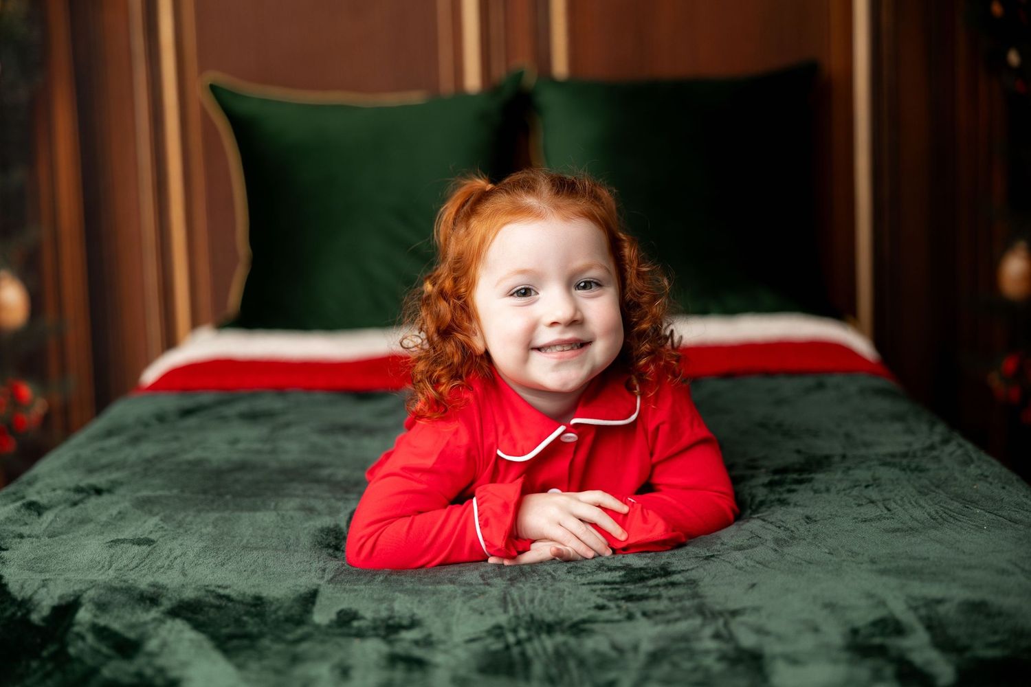 Redhead toddler in red holiday jammies on a green velvet Christmas bed at a Milk & Cookies mini session