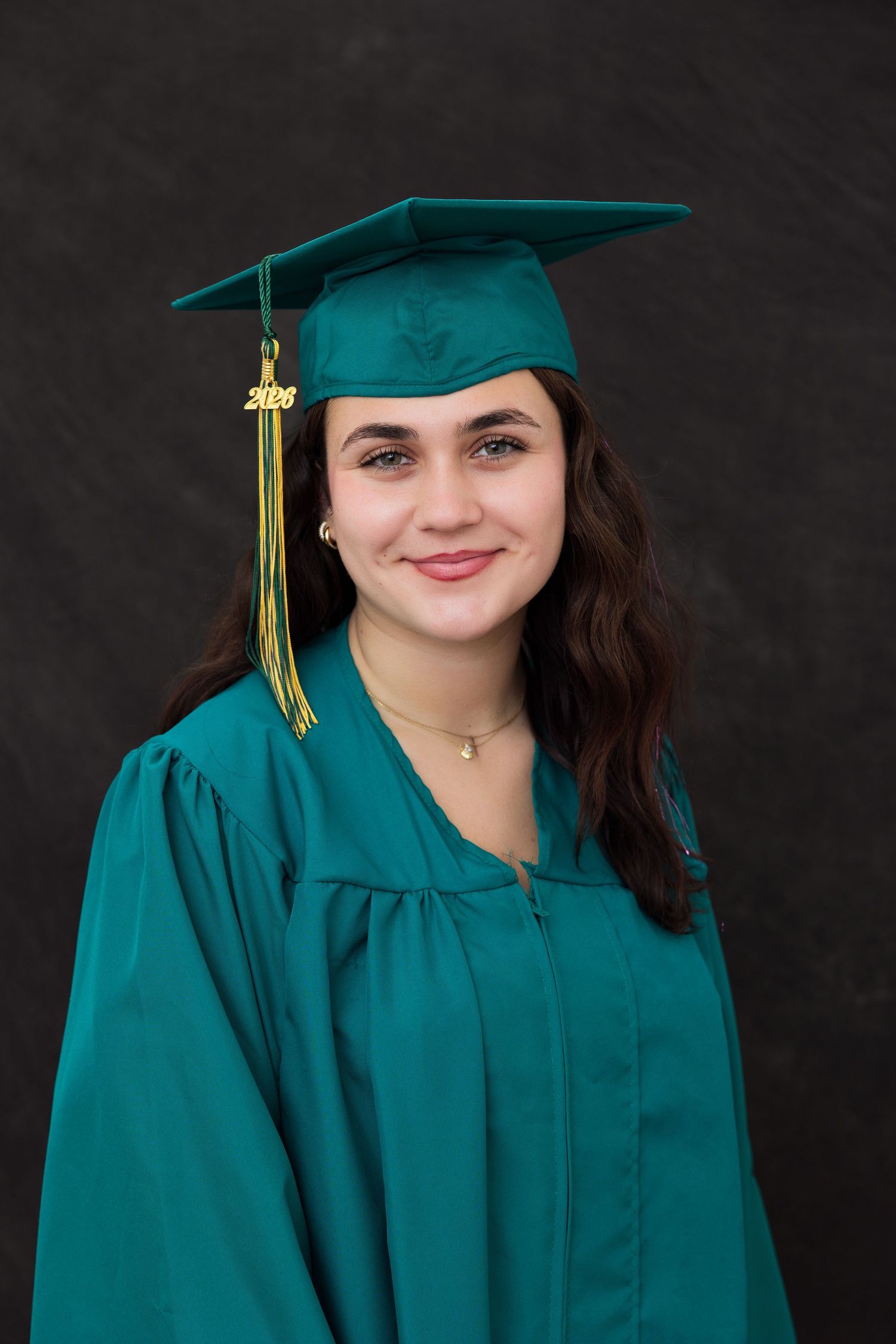 Smiling graduate in teal cap and gown with gold tassel, posing for a professional portrait photo.
