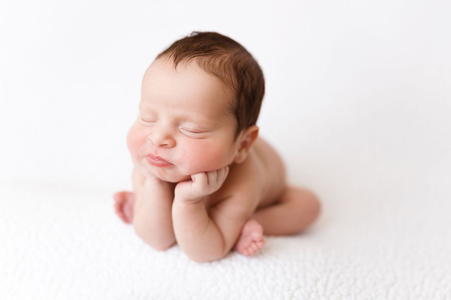 Sweet sleeping newborn baby in fetal position with hands under chin on white background.