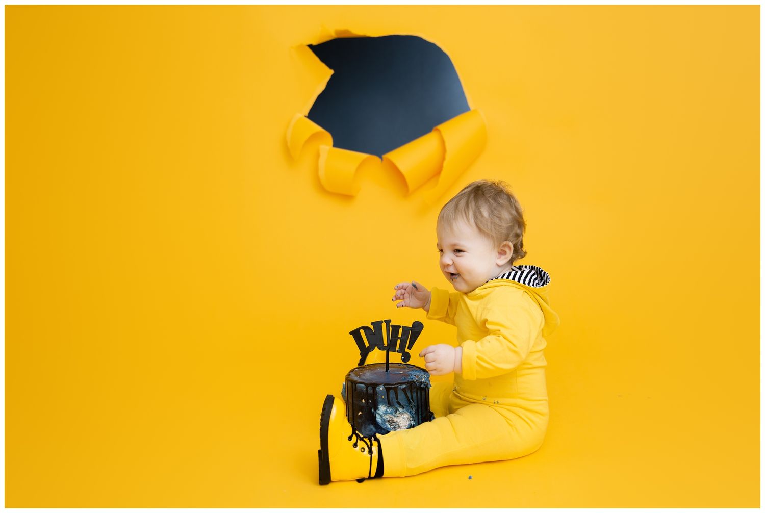Small child in bright yellow outfit tosses graduation cap against vibrant yellow background during photo session.