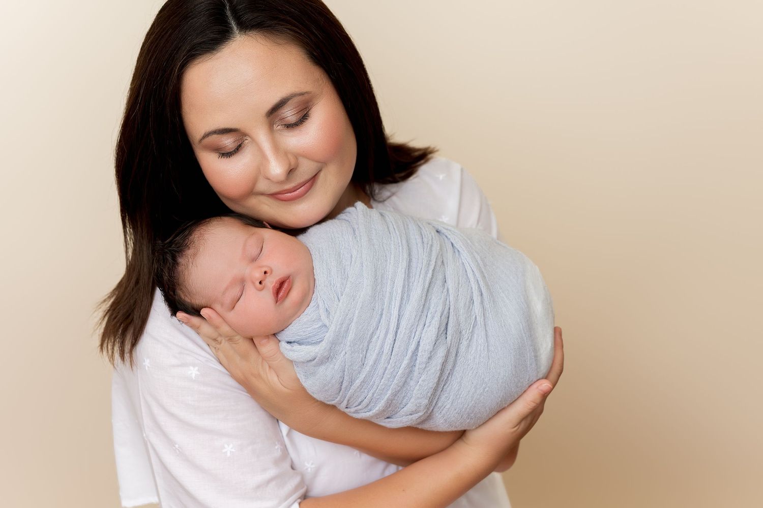 Mother gently embraces her sleeping baby in a series of tender moments captured in soft, warm lighting.