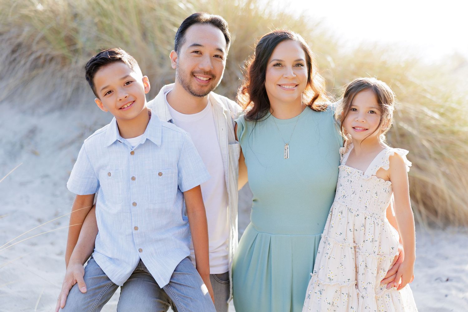 Family of four in soft blue and cream outfits on sandy beach dunes during a Santa Cruz family photo session.