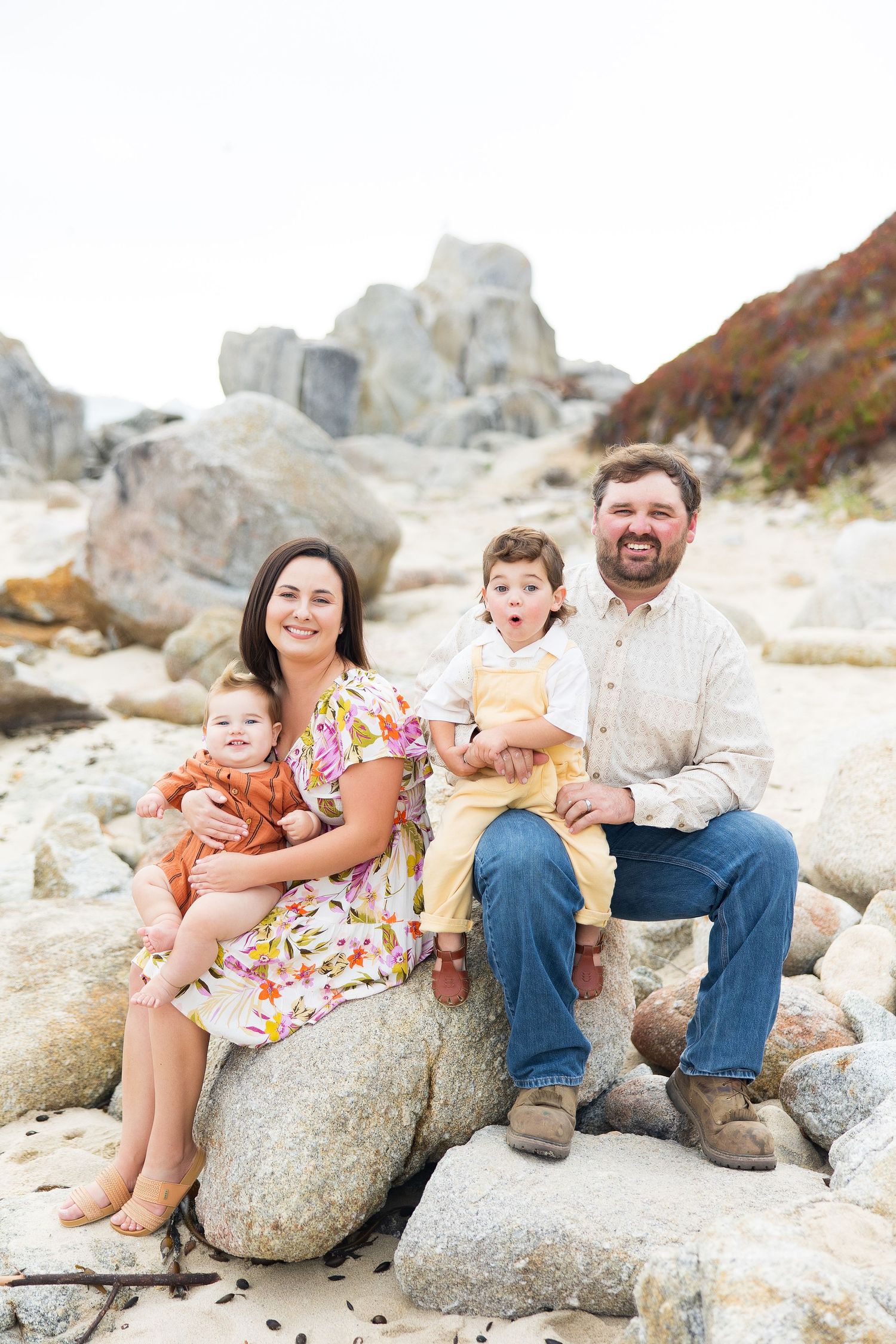Casual family portrait session on rocky beach with everyone sitting together.
