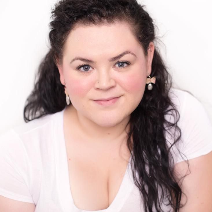 Plus-size woman in white top with dark curly hair styled half-up against white background smiling warmly at camera.