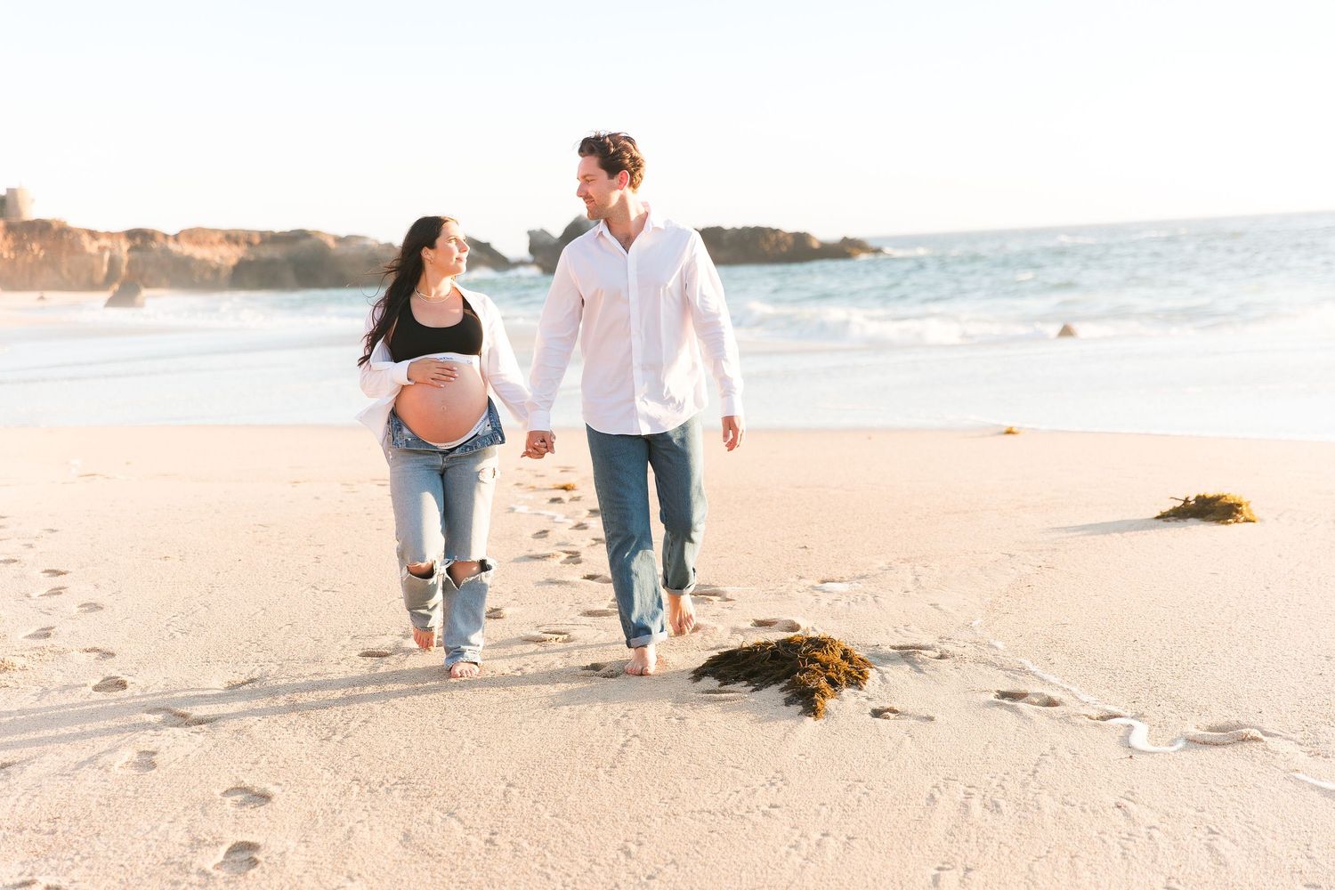 People walk together expecting a baby on a sunny beach with waves crashing on the shore in the background at Garrapata Beach.