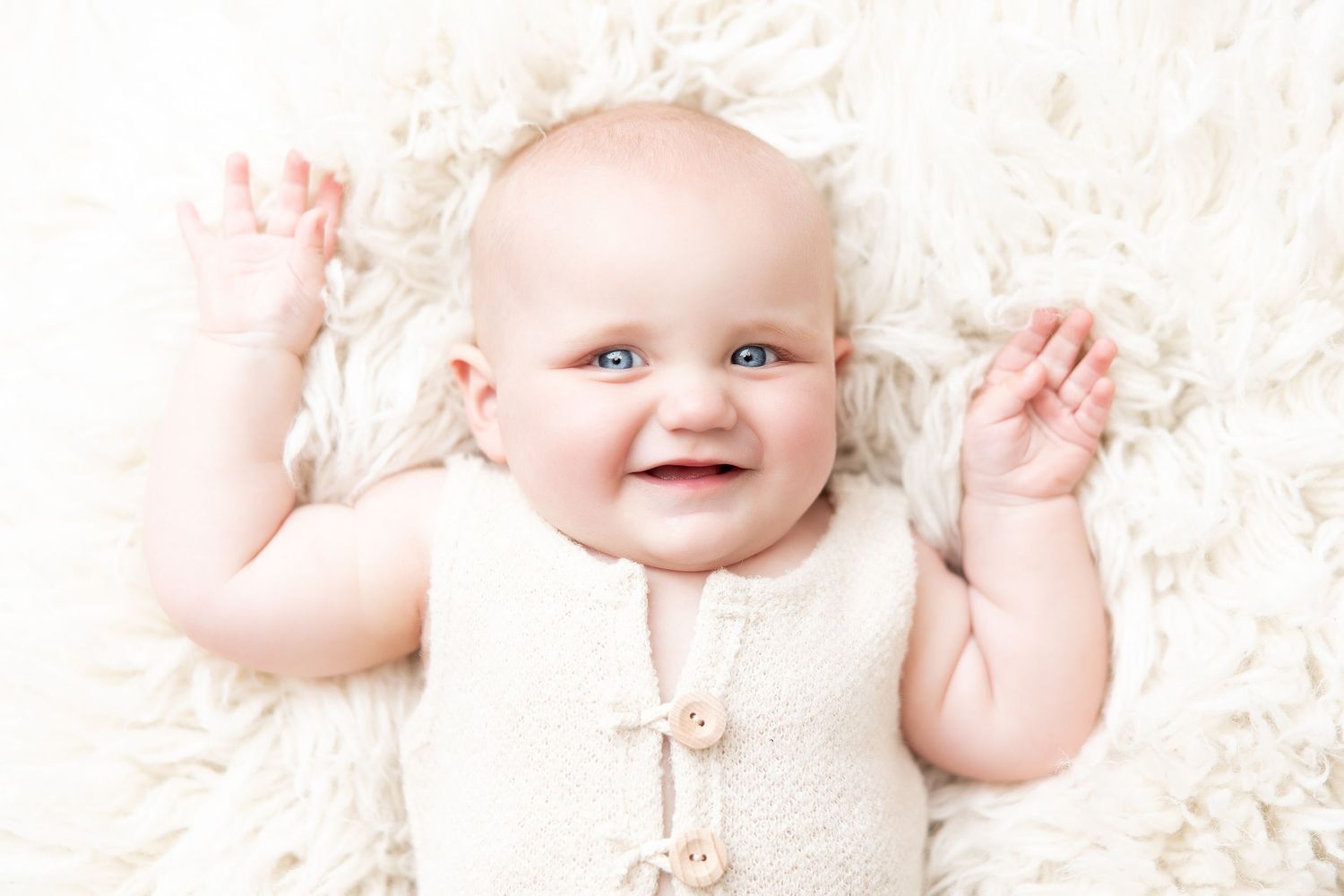 Joyful baby in cream outfit lying on white textured background.