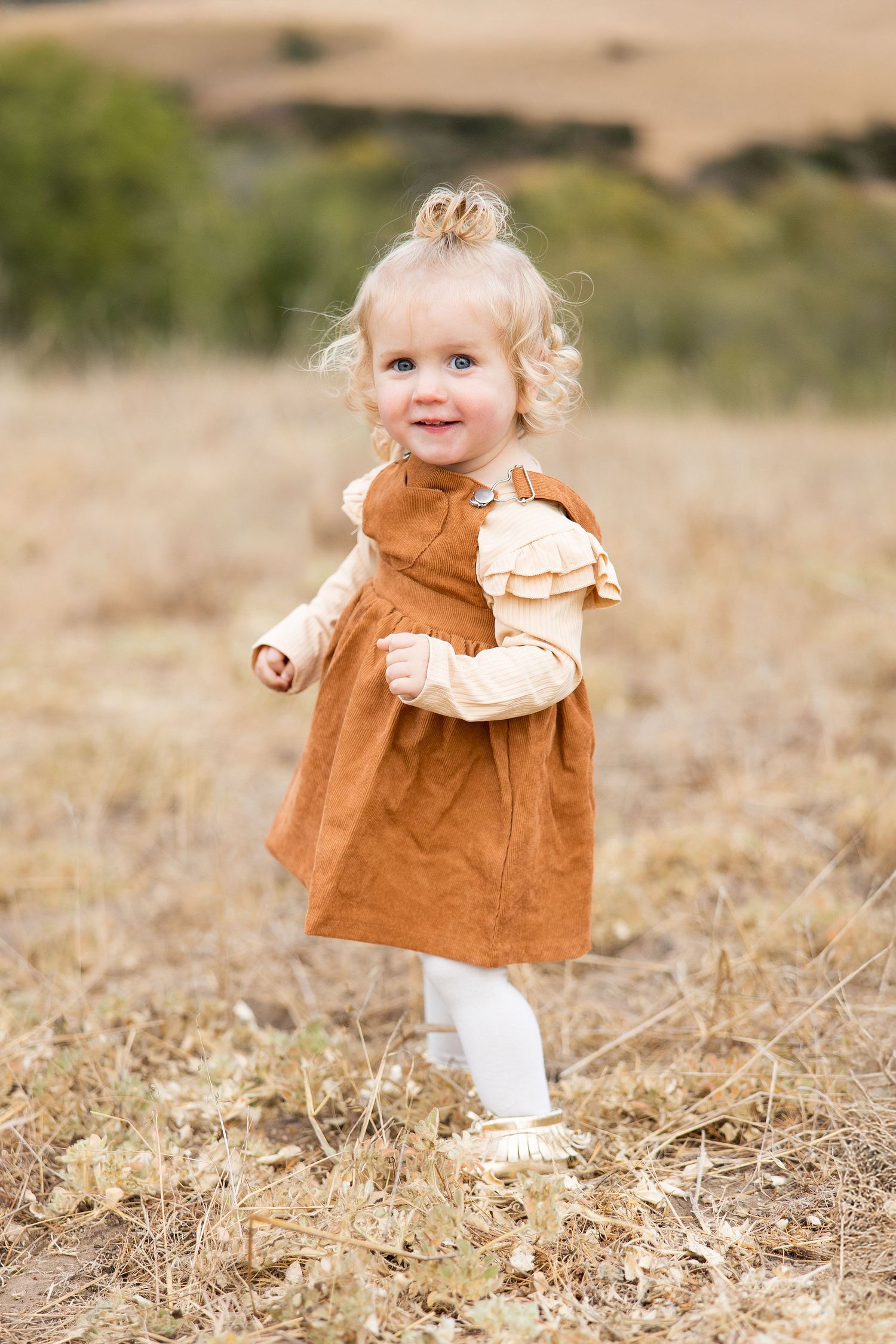 Small child in a brown dress twirls playfully in a golden field.