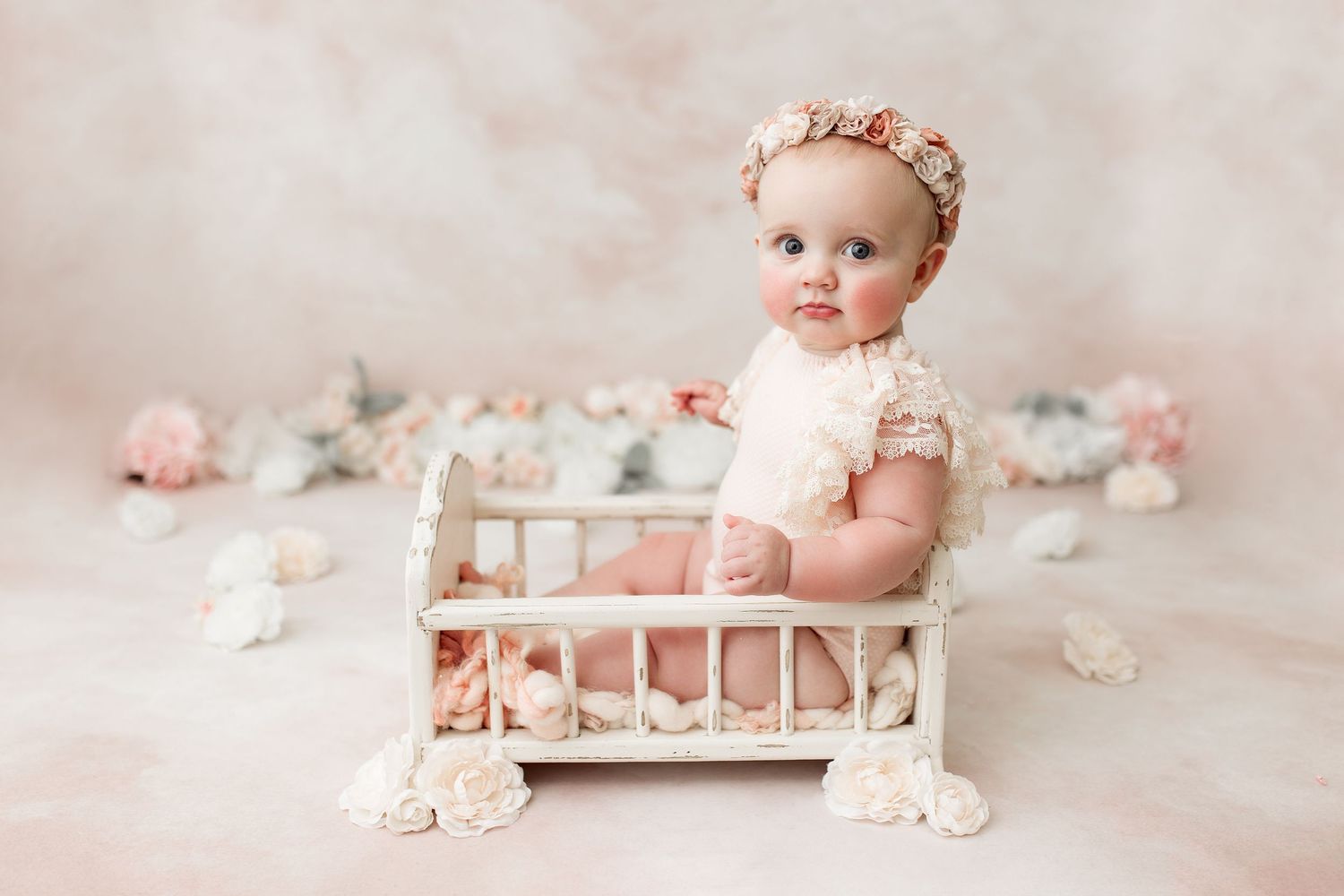 Baby posed in small white wooden crib with pink roses scattered around.