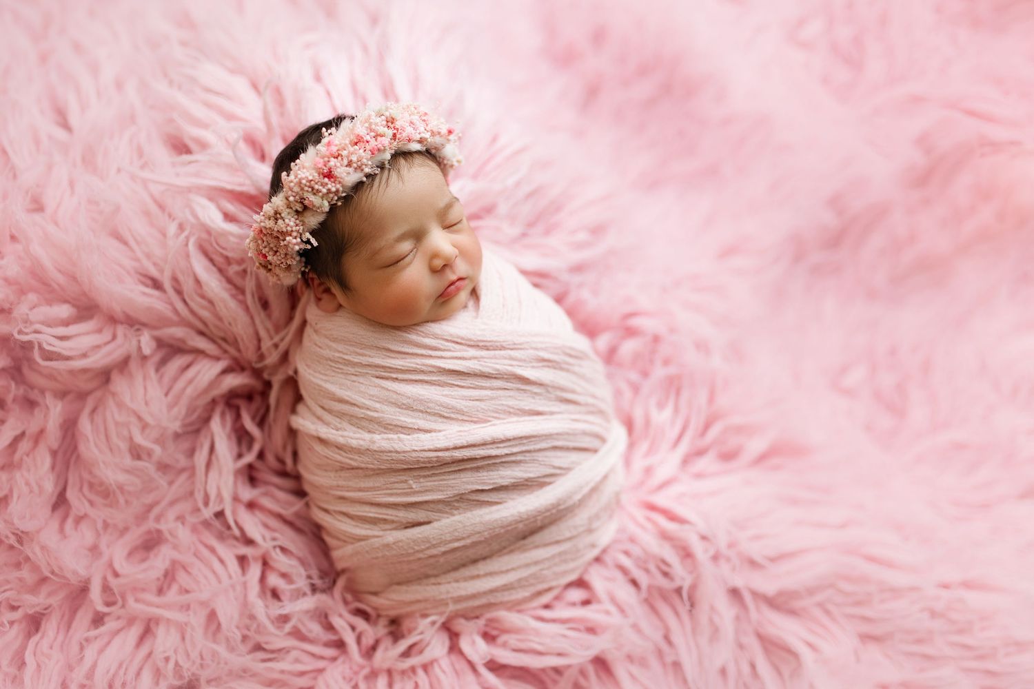Sleeping newborn on pink fluffy rug wearing delicate headband.