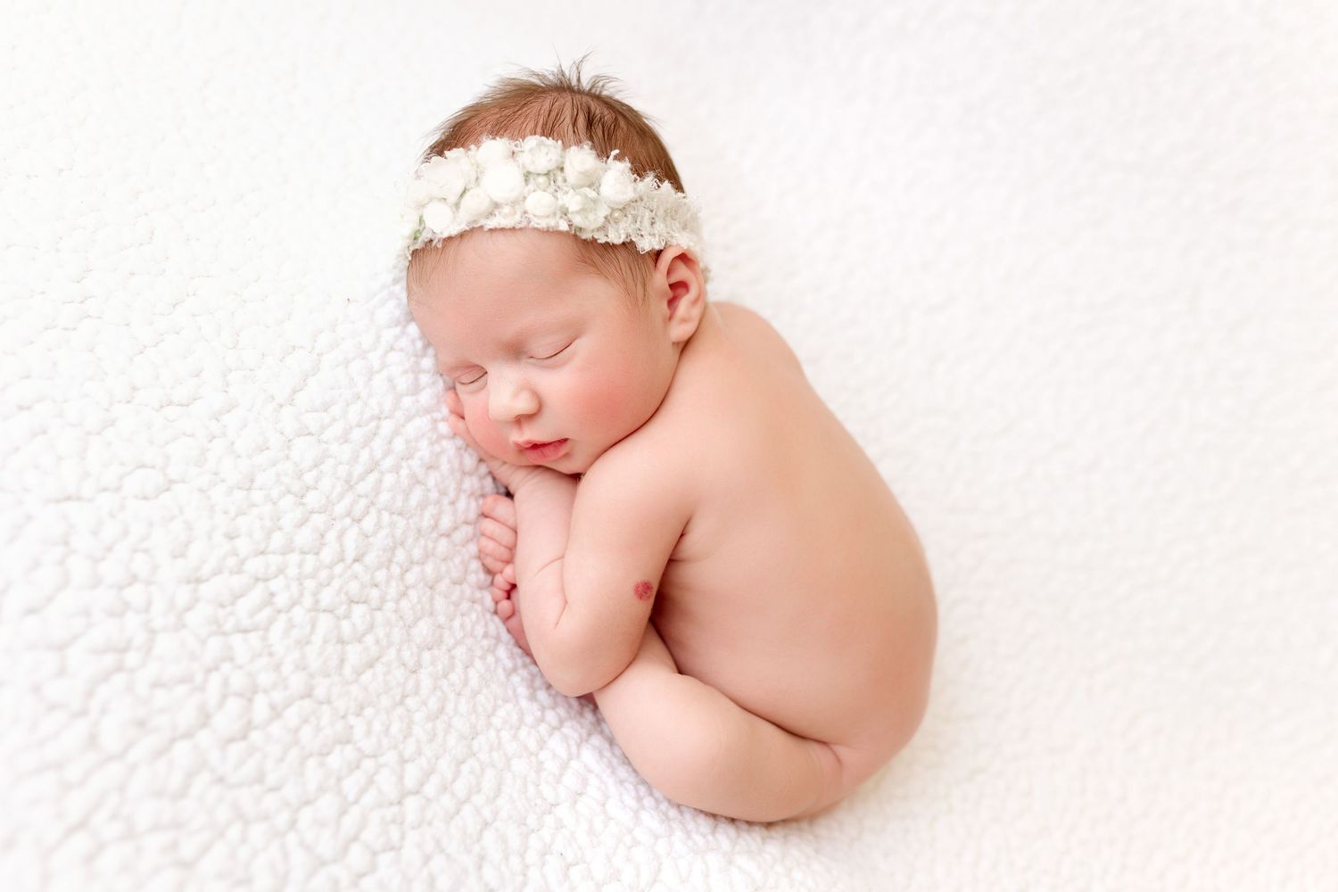 Sleeping newborn with lace headband posed on white textured background.