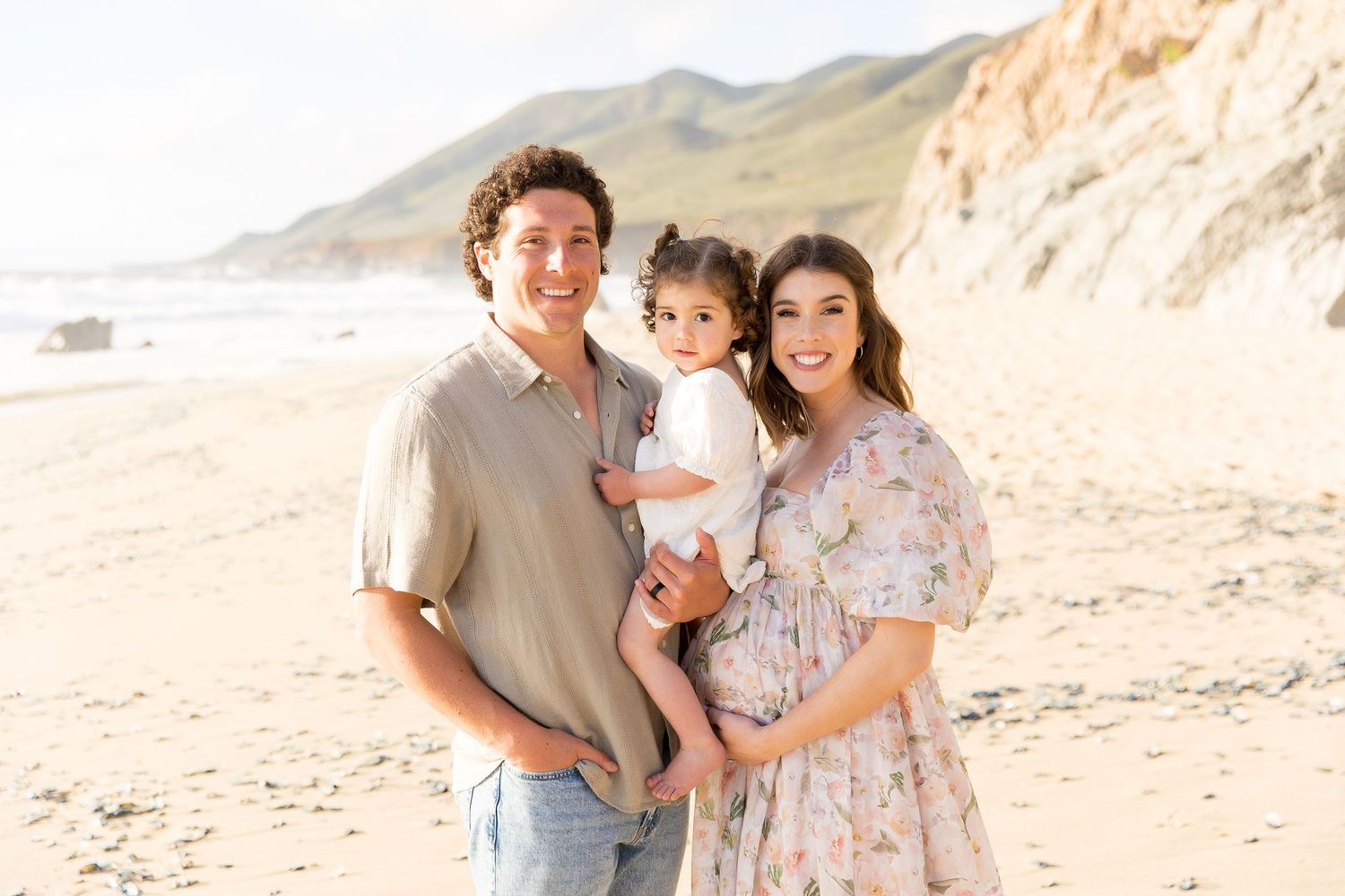 Family portrait session on a scenic beach with coastal cliffs and natural lighting.