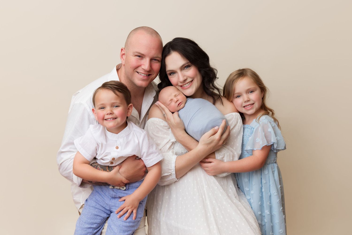 Family of four embracing and smiling in coordinated white and blue outfits.