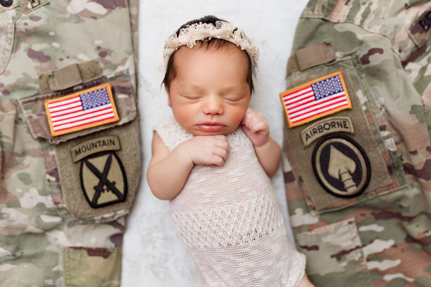 Sleeping newborn between military uniforms with American flag patches.