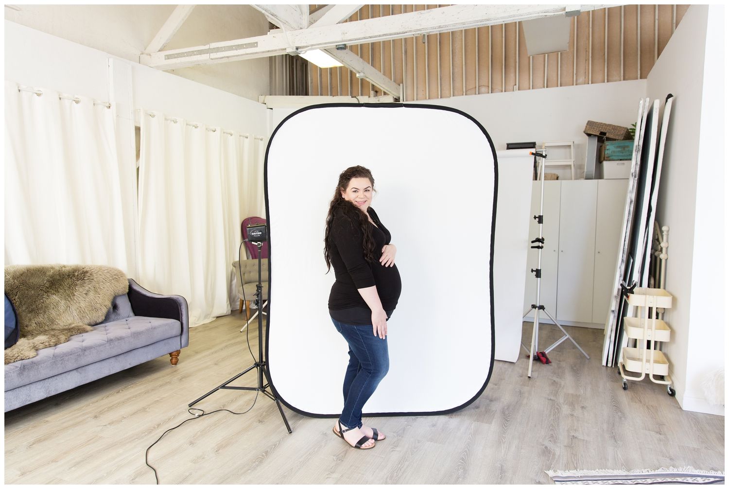Behind the scenes photo shoot setup showing a white backdrop and lighting equipment in a bright studio space.