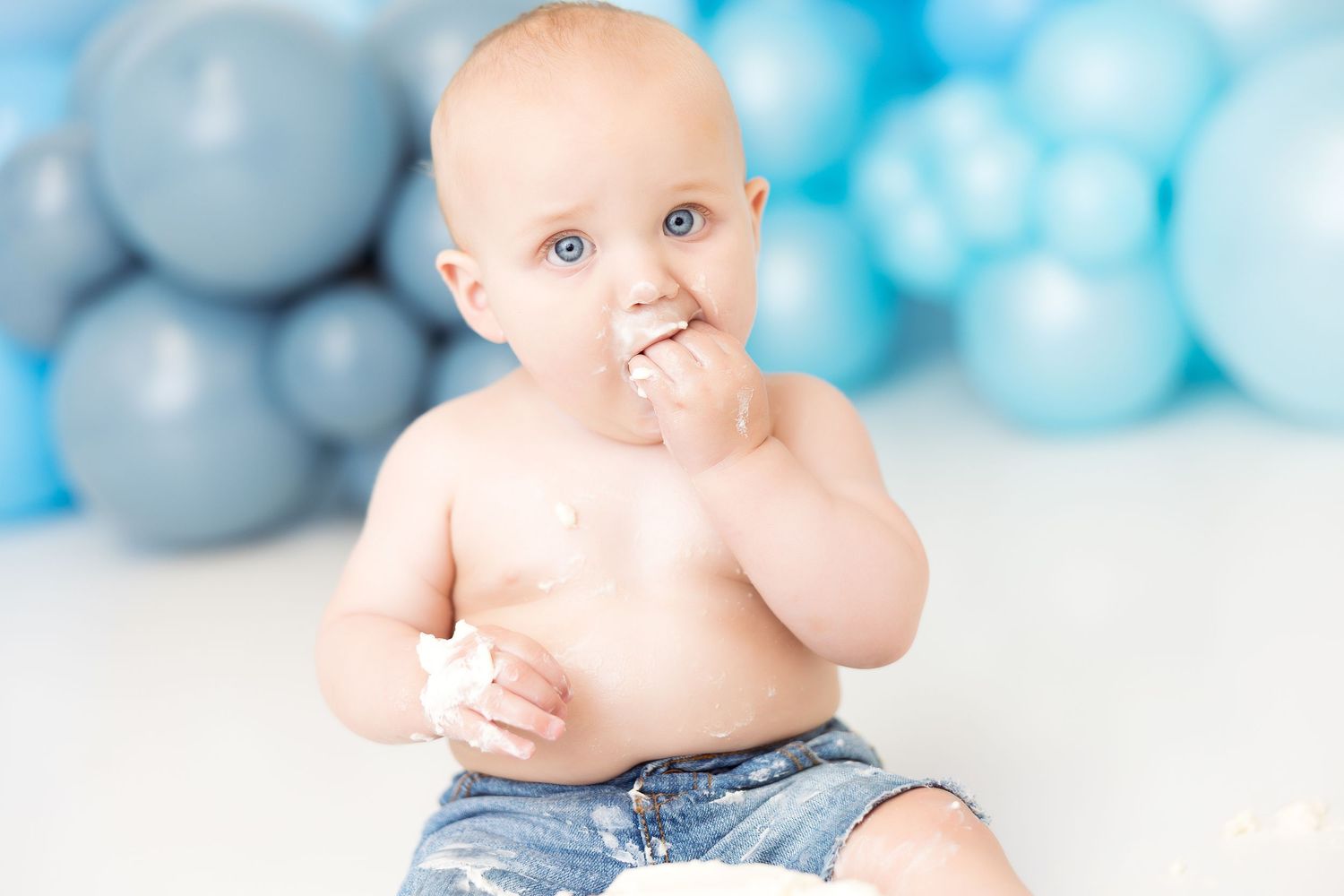 Baby in white bathtub against blue balloon backdrop for cake smash photo session.