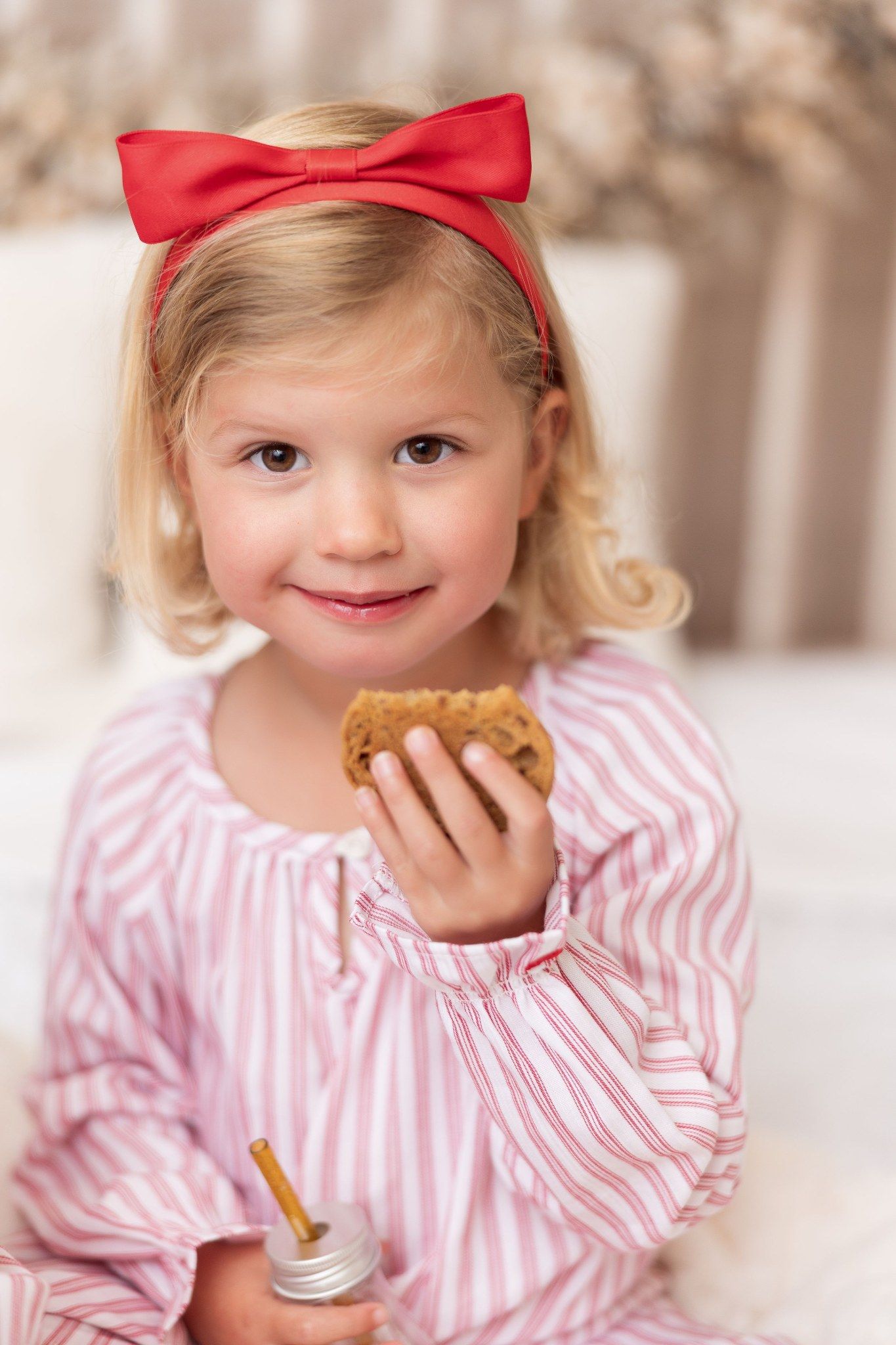 Little girl with a red bow eating a cookie at a Milk & Cookies Christmas mini session in Pacific Grove