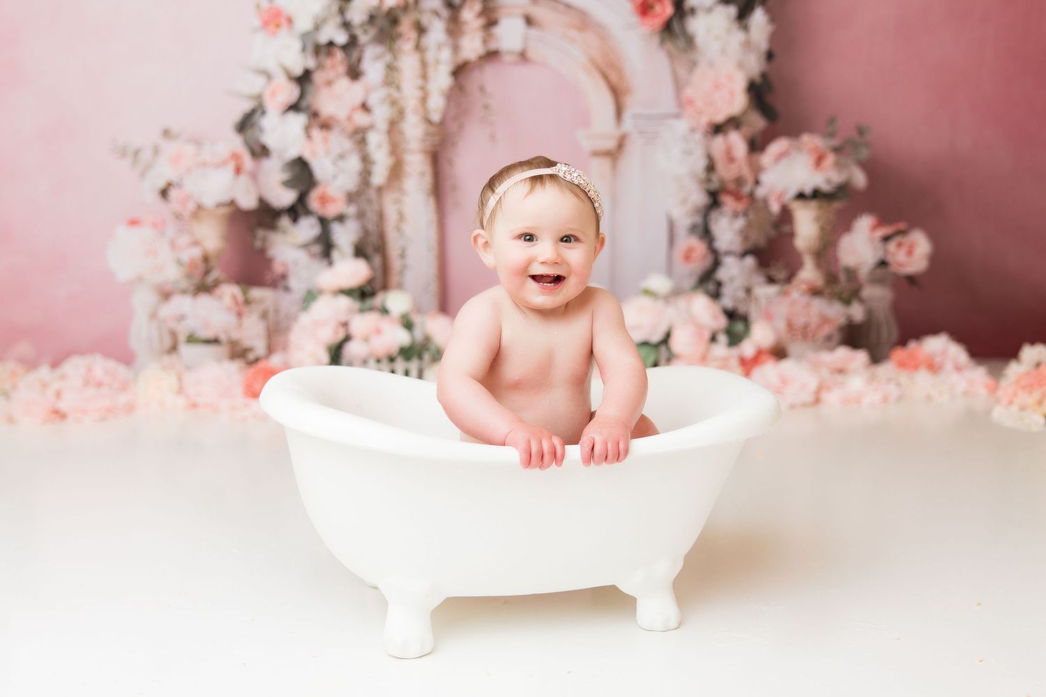 Baby portrait session in white miniature bathtub with pink floral backdrop.