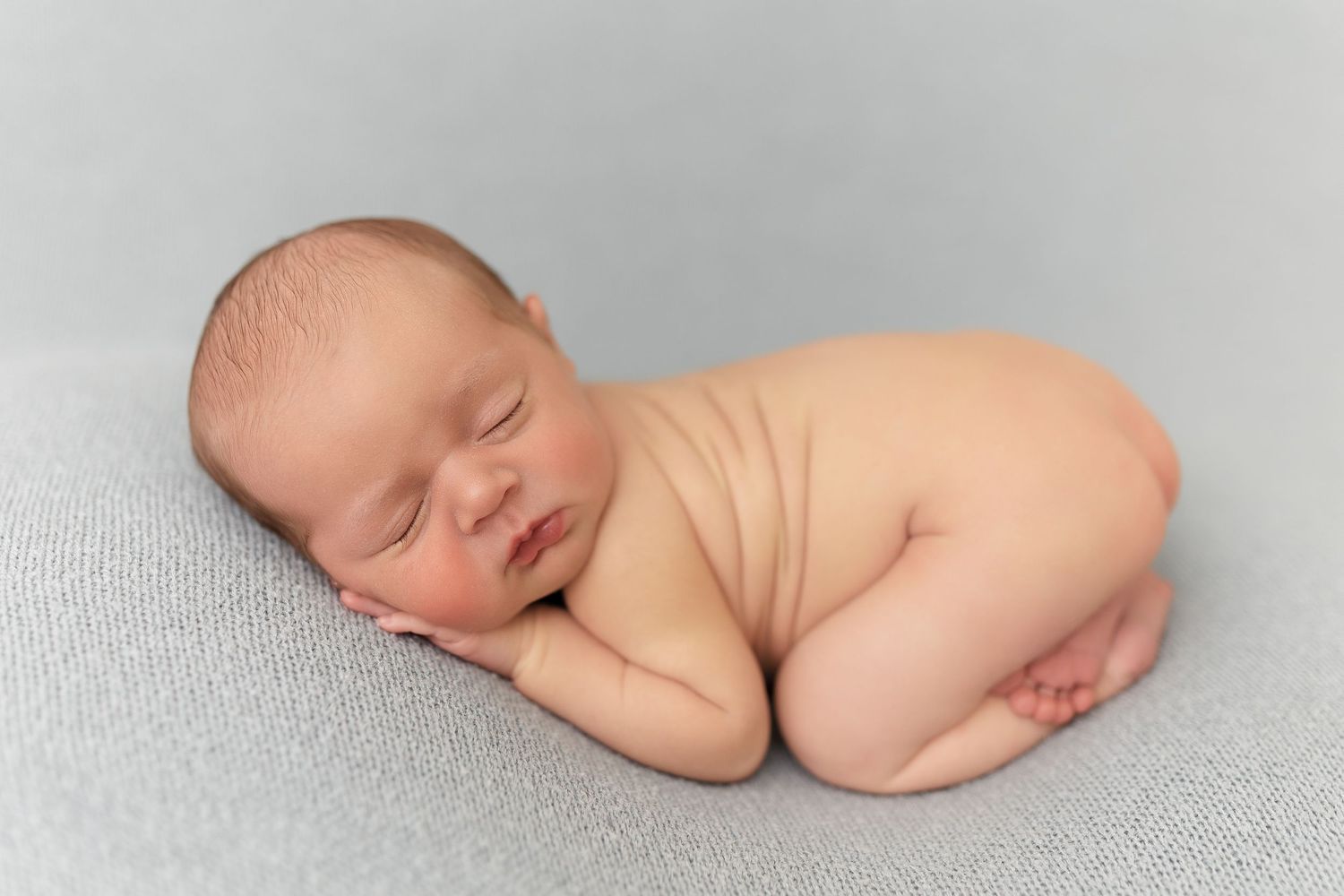 Peaceful sleeping newborn baby lying on side against gray background.
