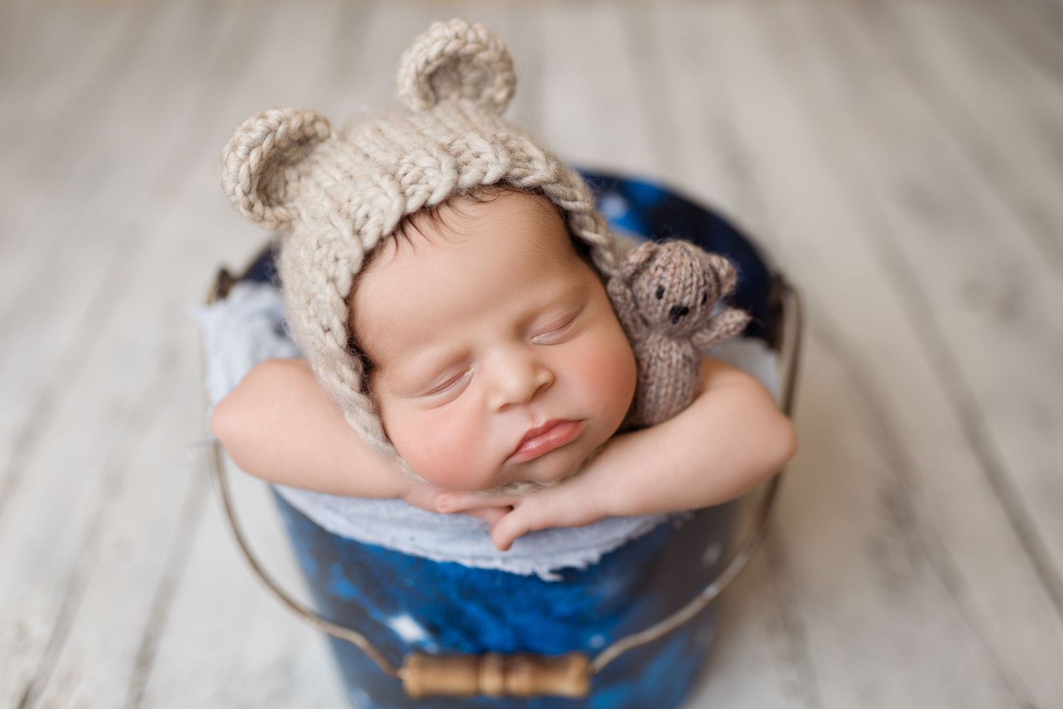 Sleeping newborn wearing knit hat rests in blue vintage bowl.