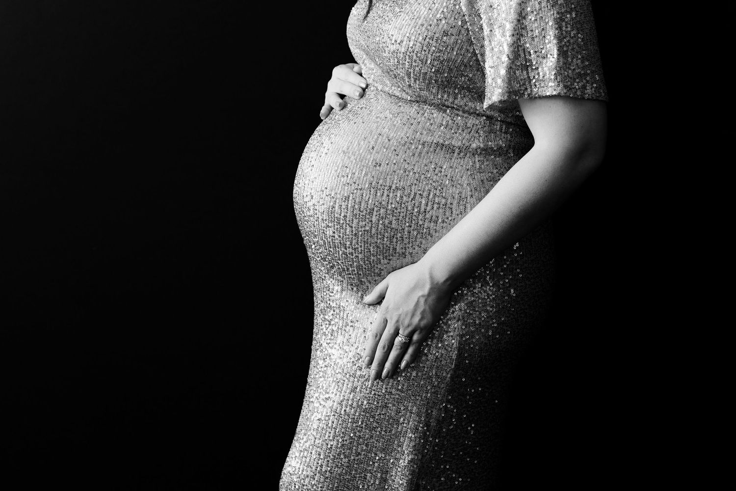 Black and white close-up of pregnant belly in glittering evening dress.