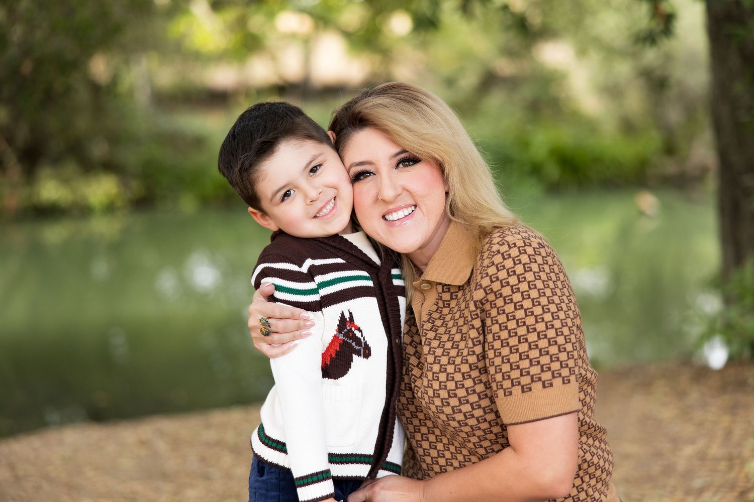 A mother and child share a warm embrace while sitting outdoors in a natural park setting with soft lighting.