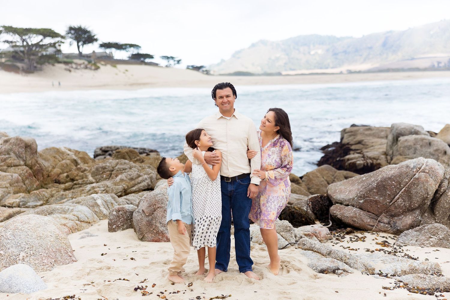 Family enjoying time together on rocky beach with mountains in background.