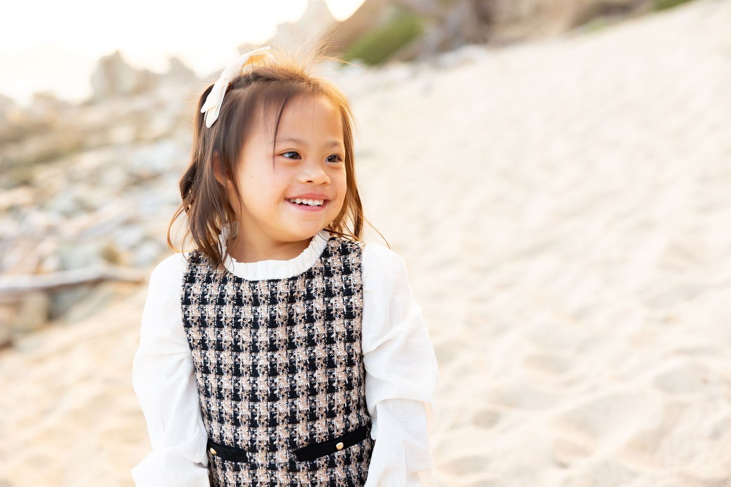 Child in houndstooth dress posing on sandy beach during family photoshoot.