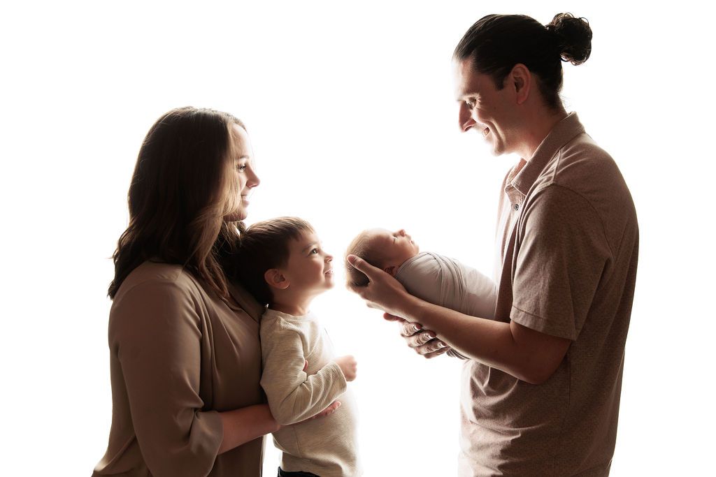 A silhouetted family of three sharing a joyful moment together against a bright white background.