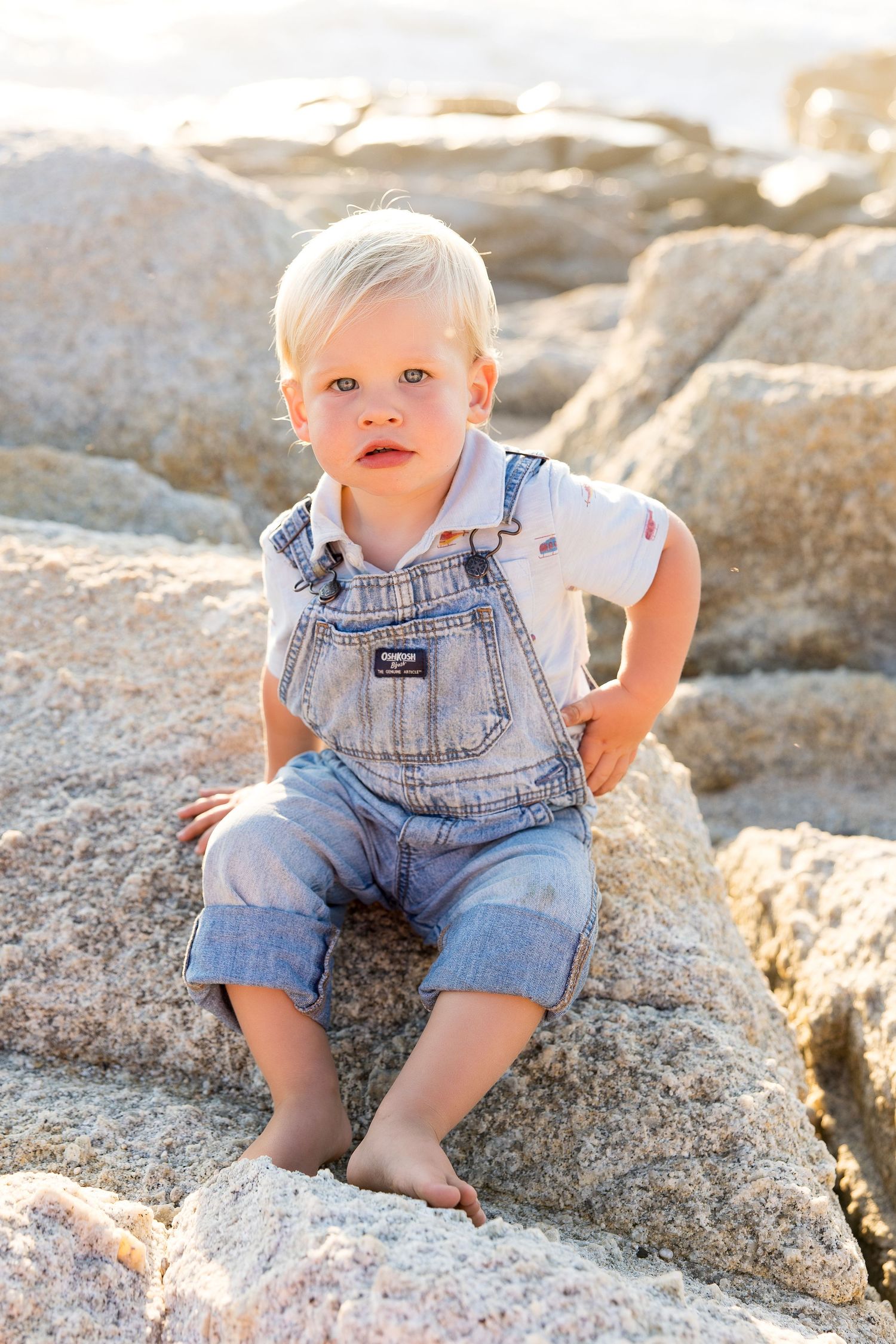 Baby in denim overalls explores rocky terrain at the beach.