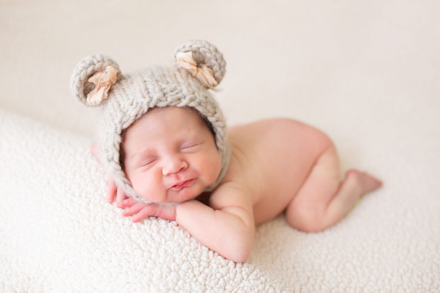 A sleeping newborn baby lies peacefully on soft white fabric in a series of gentle poses.