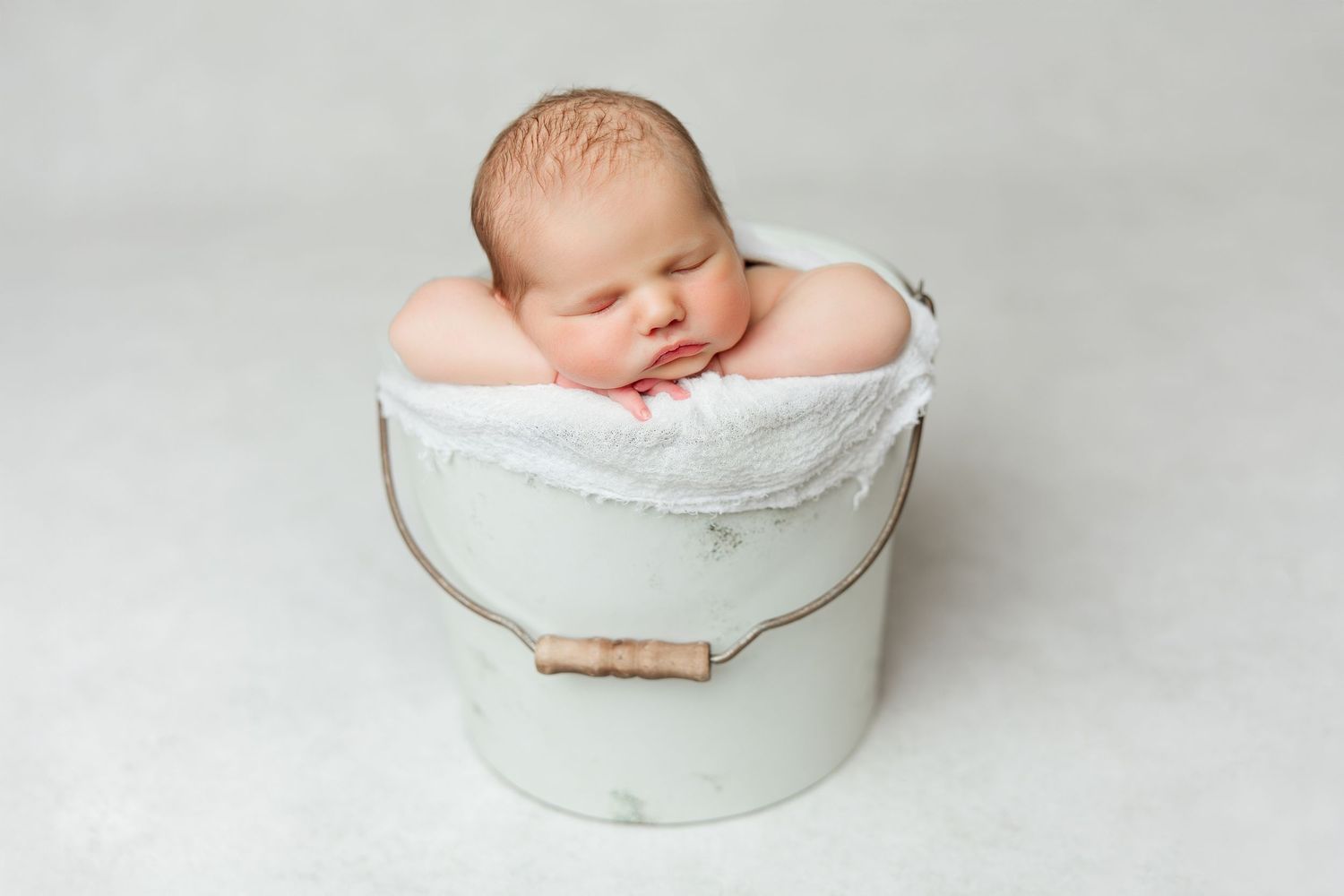 A sleeping newborn baby nestled in a white ceramic bowl against a light background.