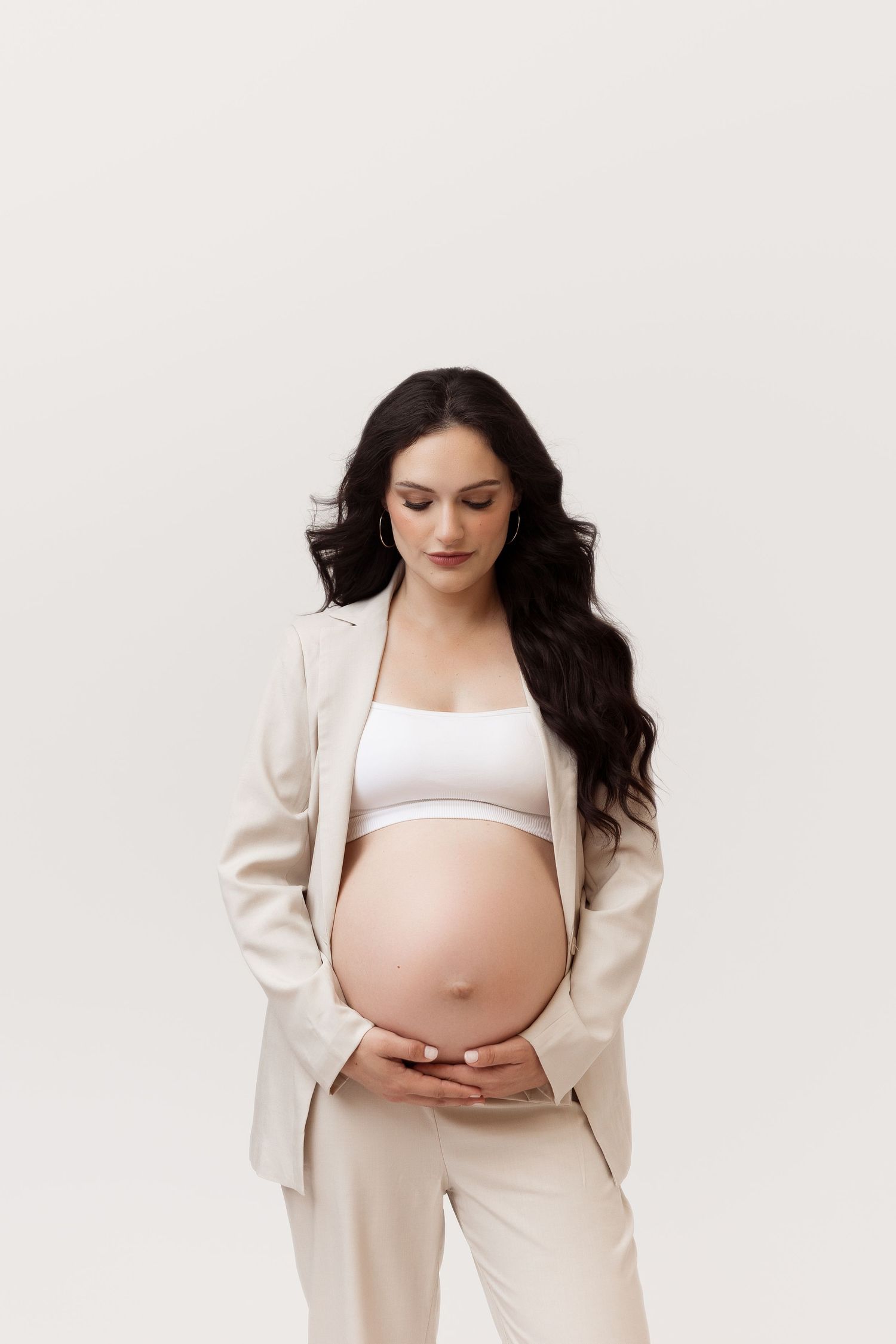 Elegant maternity portraits in cream colored business attire against white backdrop.
