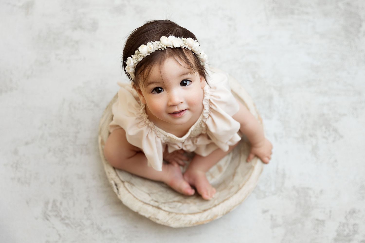 Baby in cream lace dress poses in vintage bowl for portrait session.