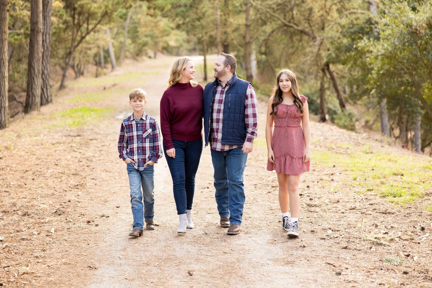 Family of four walks together on a scenic forest trail during an autumn day.