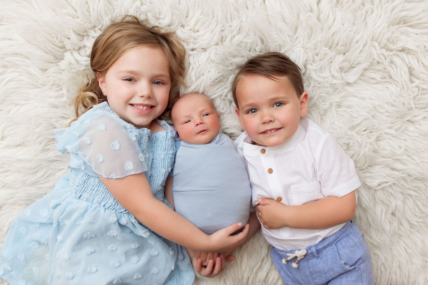 Family portrait of siblings on fluffy white rug.