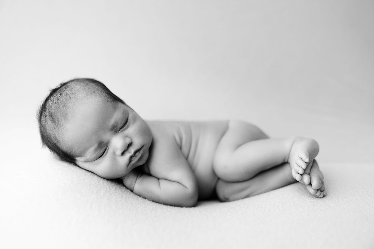 Peaceful black and white portrait of a sleeping newborn baby laying on their side.