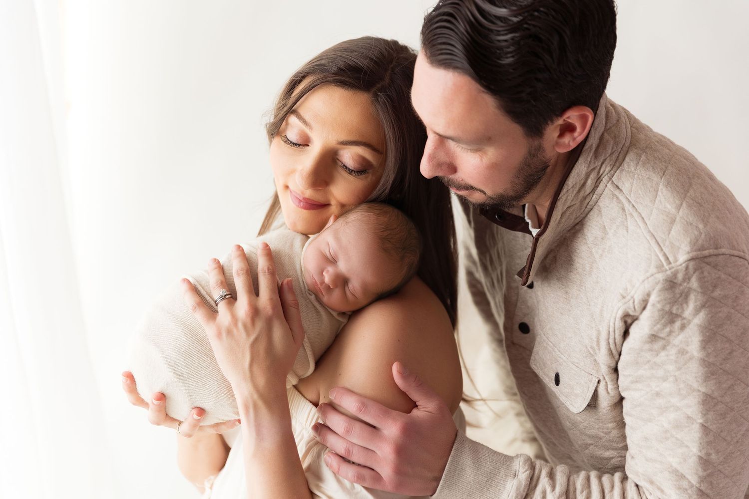 Parents sharing an intimate bonding moment with their newborn baby in a warm natural light setting.