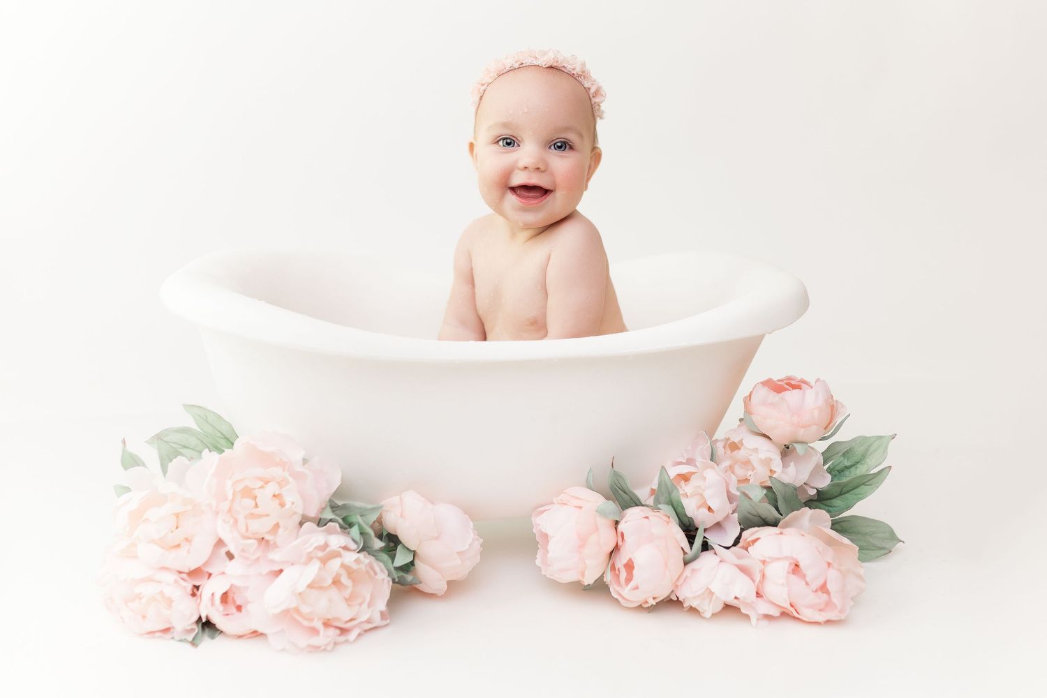 A sweet studio portrait featuring a small baby in a white bathtub surrounded by pink roses.
