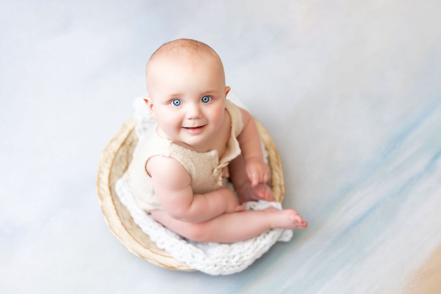 Cheerful baby sitting in wooden bowl against blue and white background.