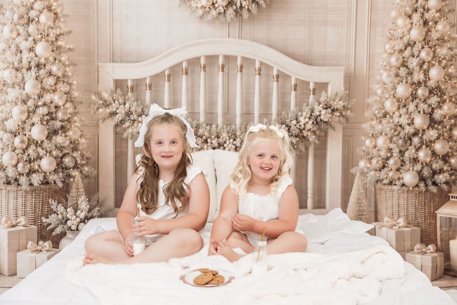 Two sisters in white Christmas pajamas on the neutral, gold and white Milk and Cookies Christmas bed set at a Pacific Grove studio