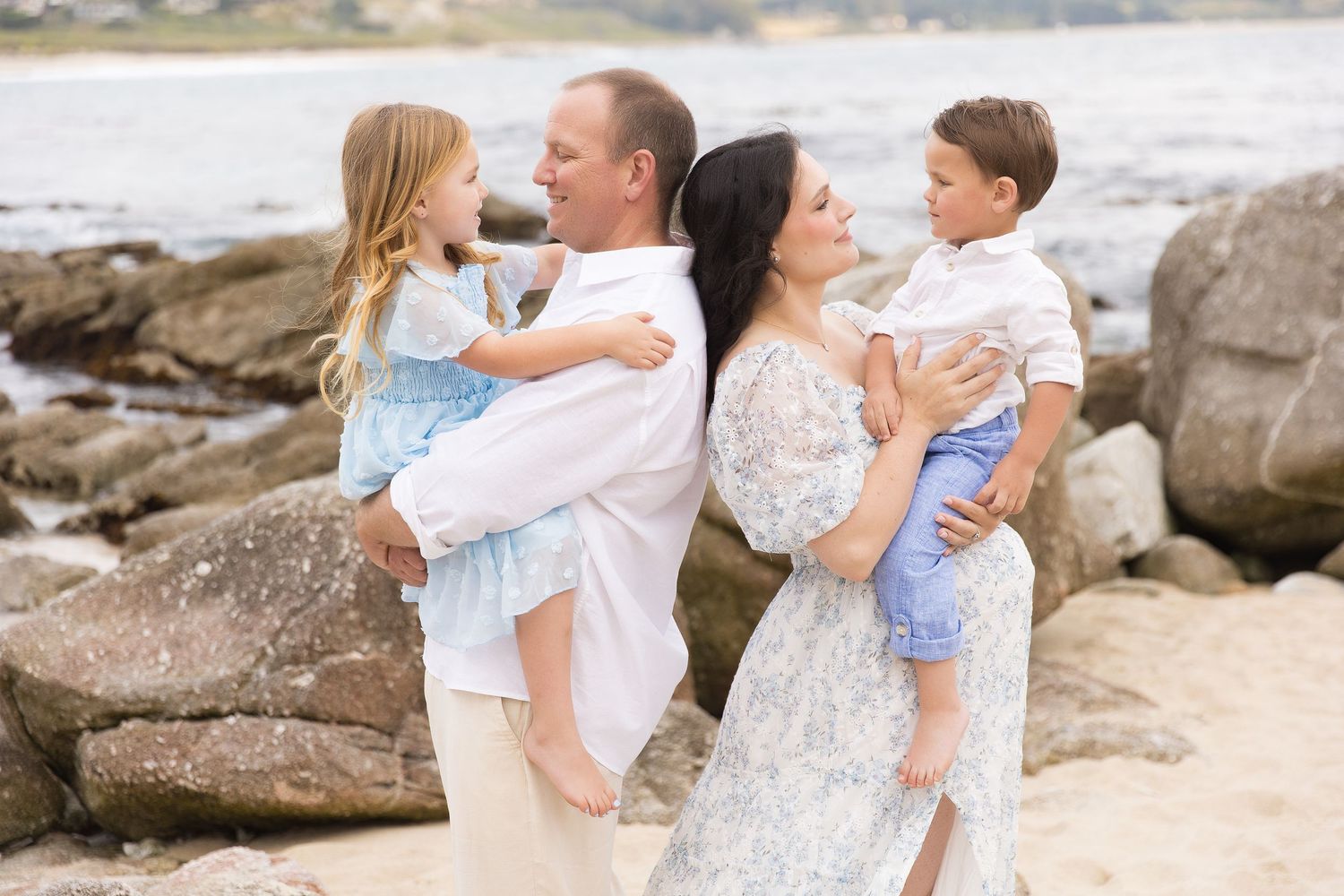 Loving family embraces on rocky beach during golden hour portrait session.