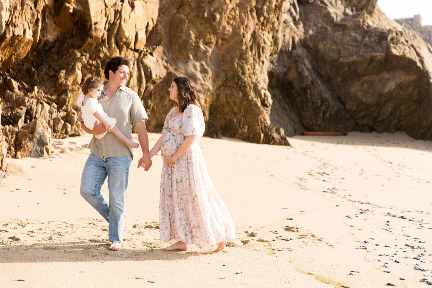 Beach photoshoot near rocky cliffs during golden hour.